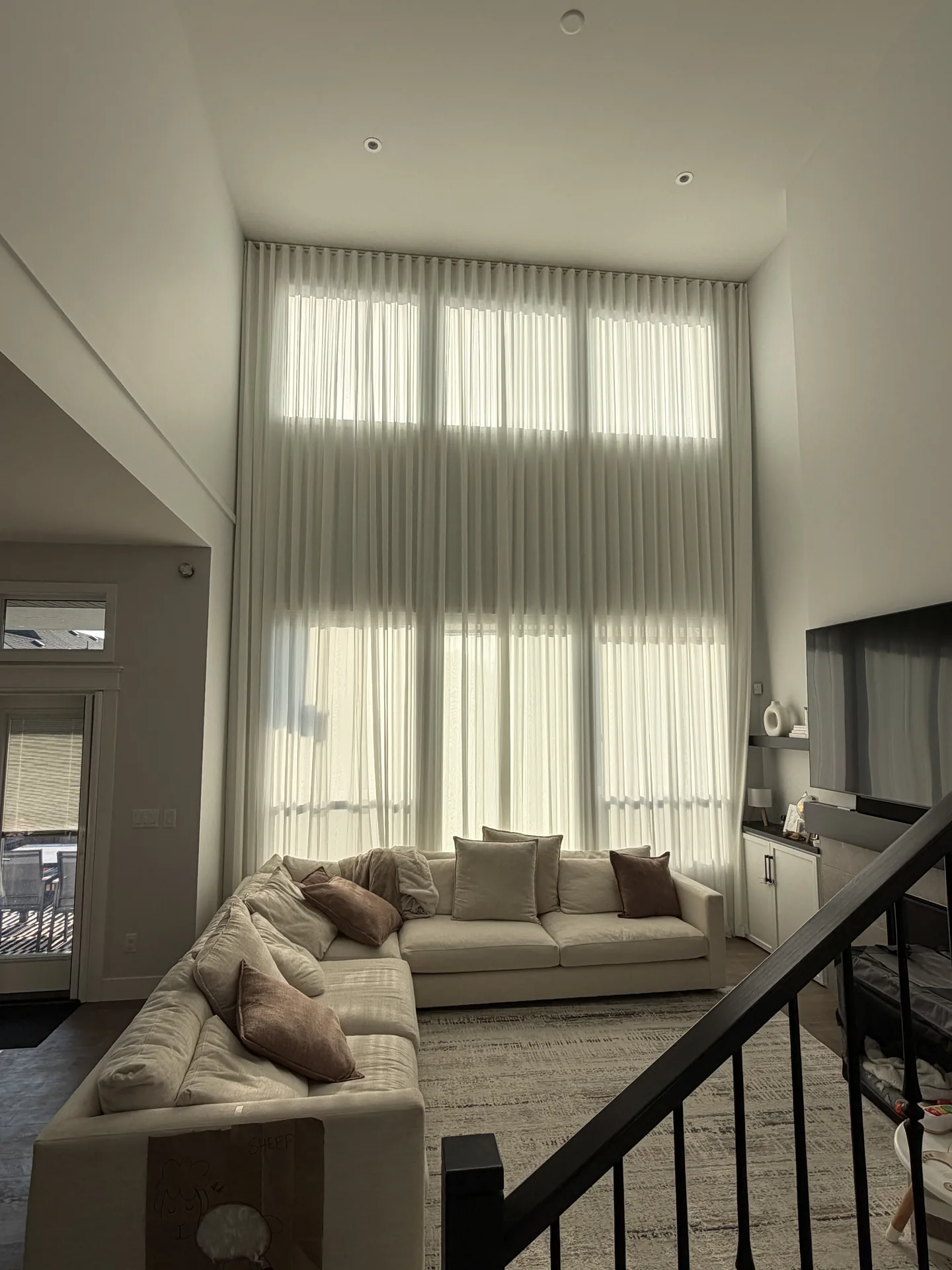 Double-height window covered with softly pleated sheer drapes