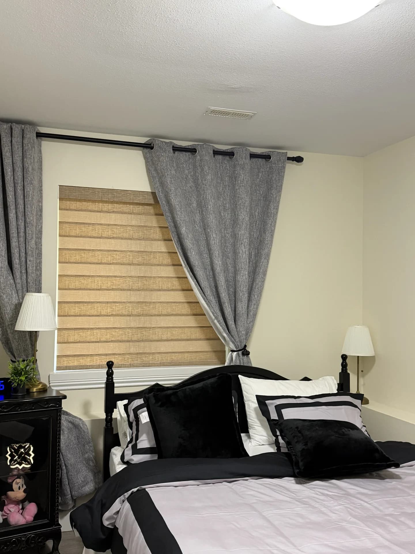 Layered zebra blind framed by grey bedroom curtains
